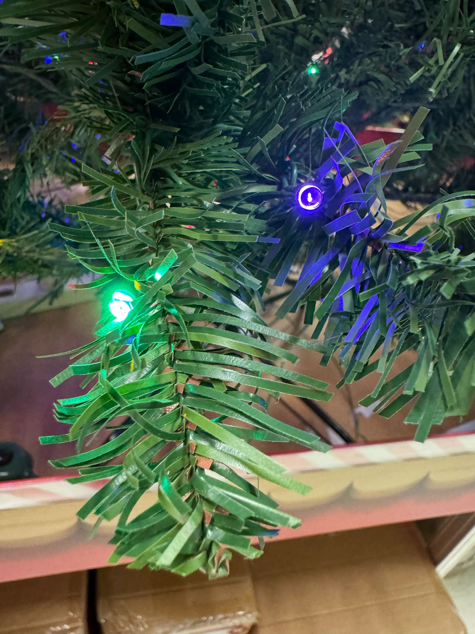 Close-up of sparse PVC spruce branches with scattered multicolor mini lights; visible gaps between thin tips, underwhelming light coverage