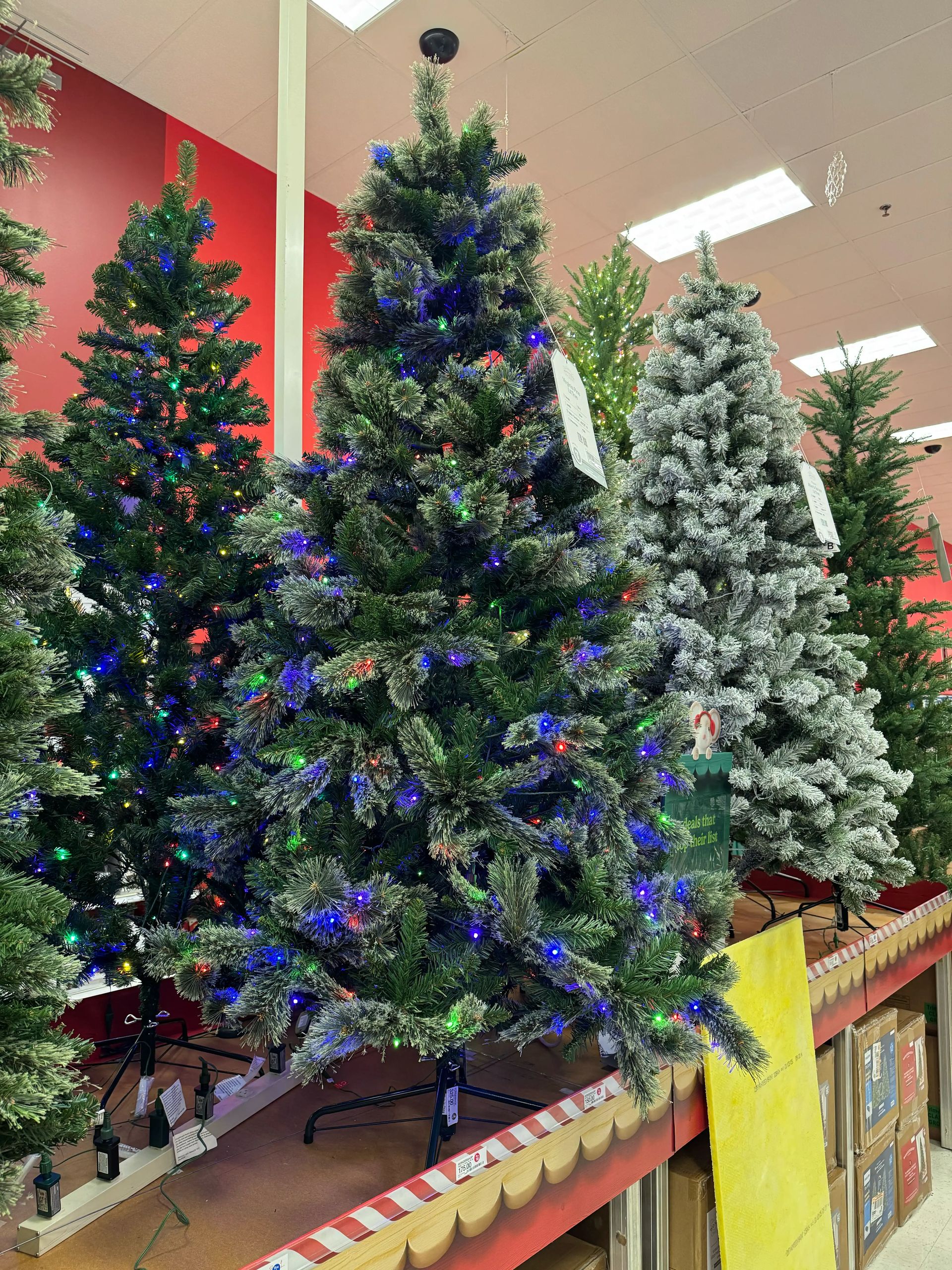 Budget PVC pine tree with sparse branching, visible gaps throughout, multicolor mini bulbs concentrated at branch tips, underwhelming fullness for display