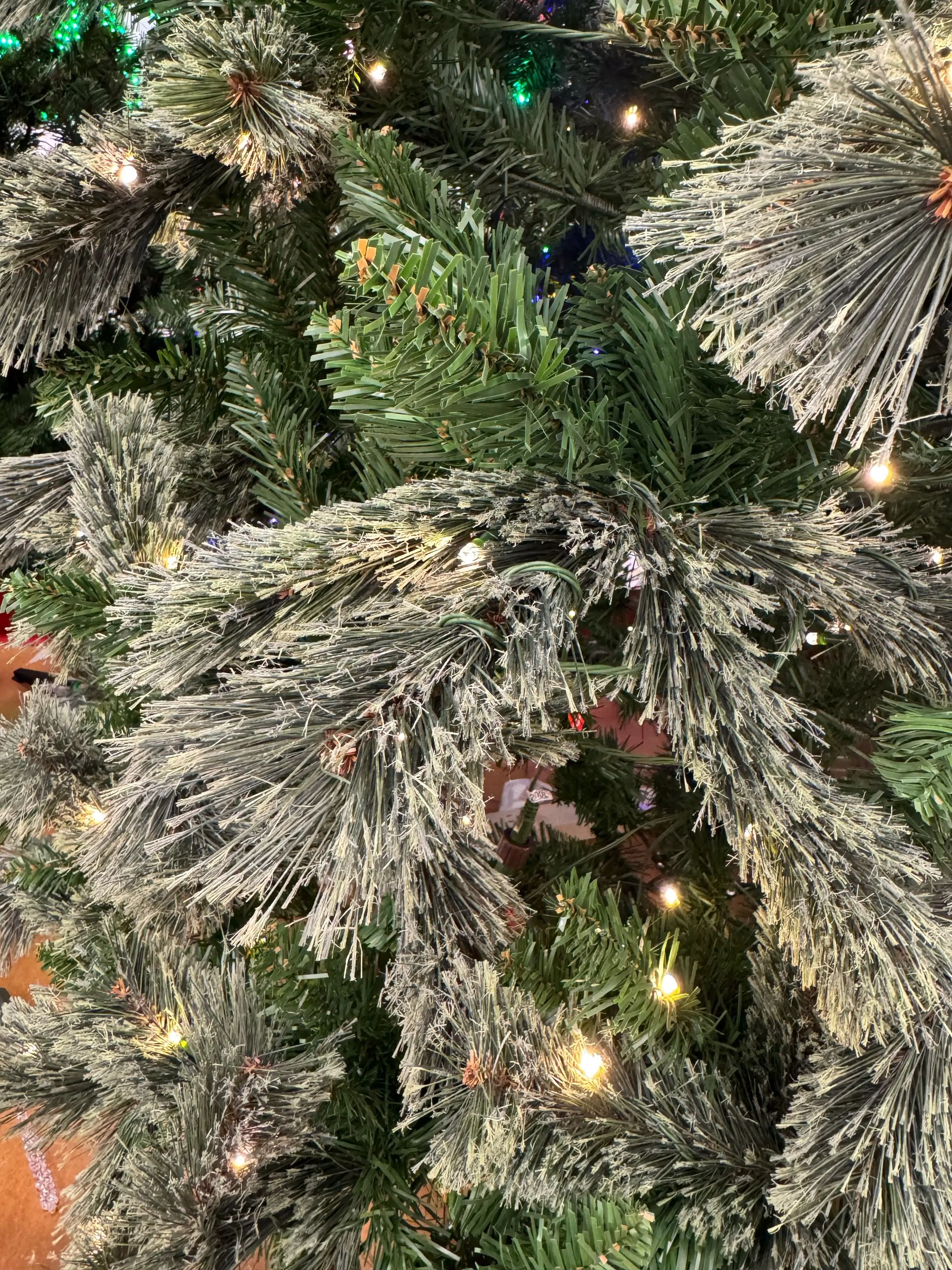 Close-up of pine-style tree showing frosted white branch tips with sparse traditional PVC needles, warm LED lights, and visible green inner branches throughout