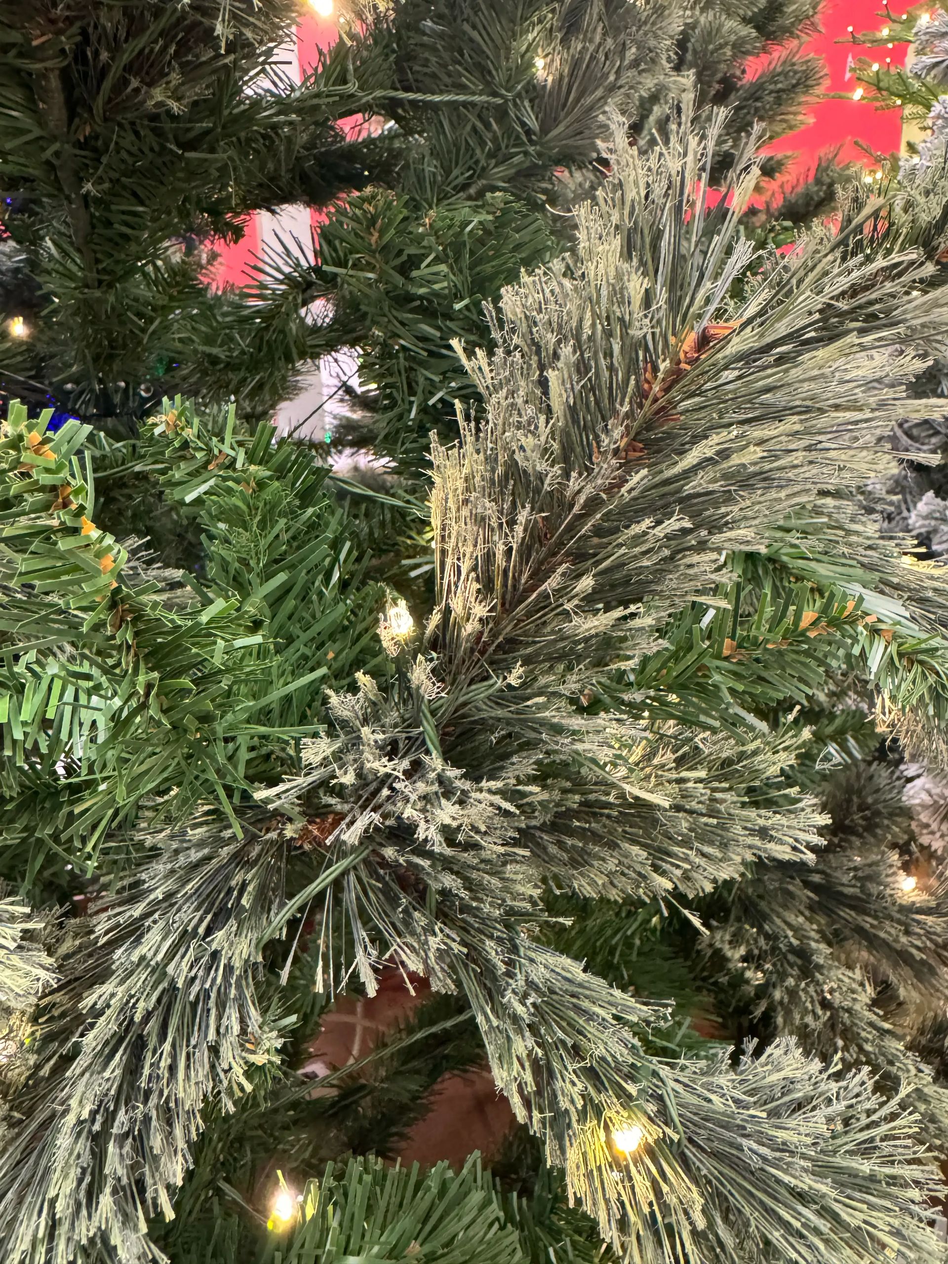 Close-up of sparse PVC pine branches with frosted tips, thin needle coverage, visible gaps, modest warm LED spacing throughout