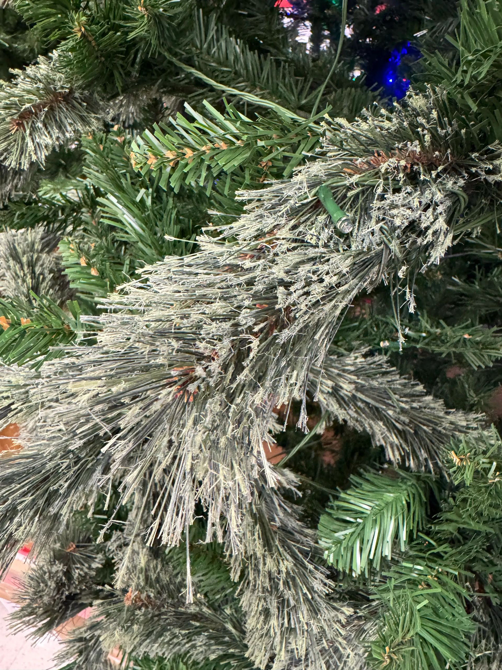 Close-up of sparse PVC pine branches with heavy frosting/flocking, visible wiring, modest light coverage, budget construction