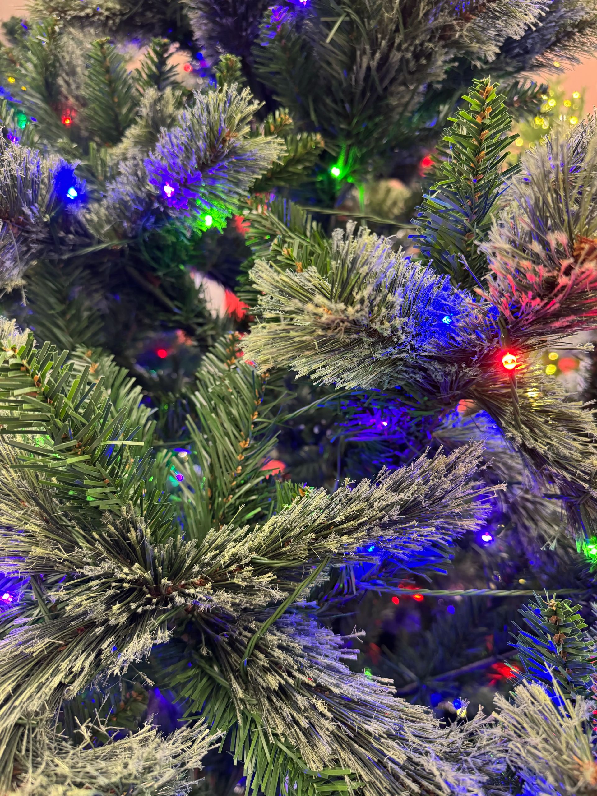 Close-up of pine-style tree with traditional PVC needles, sparse multicolor mini bulb coverage, visible dark gaps between branches, budget construction quality.