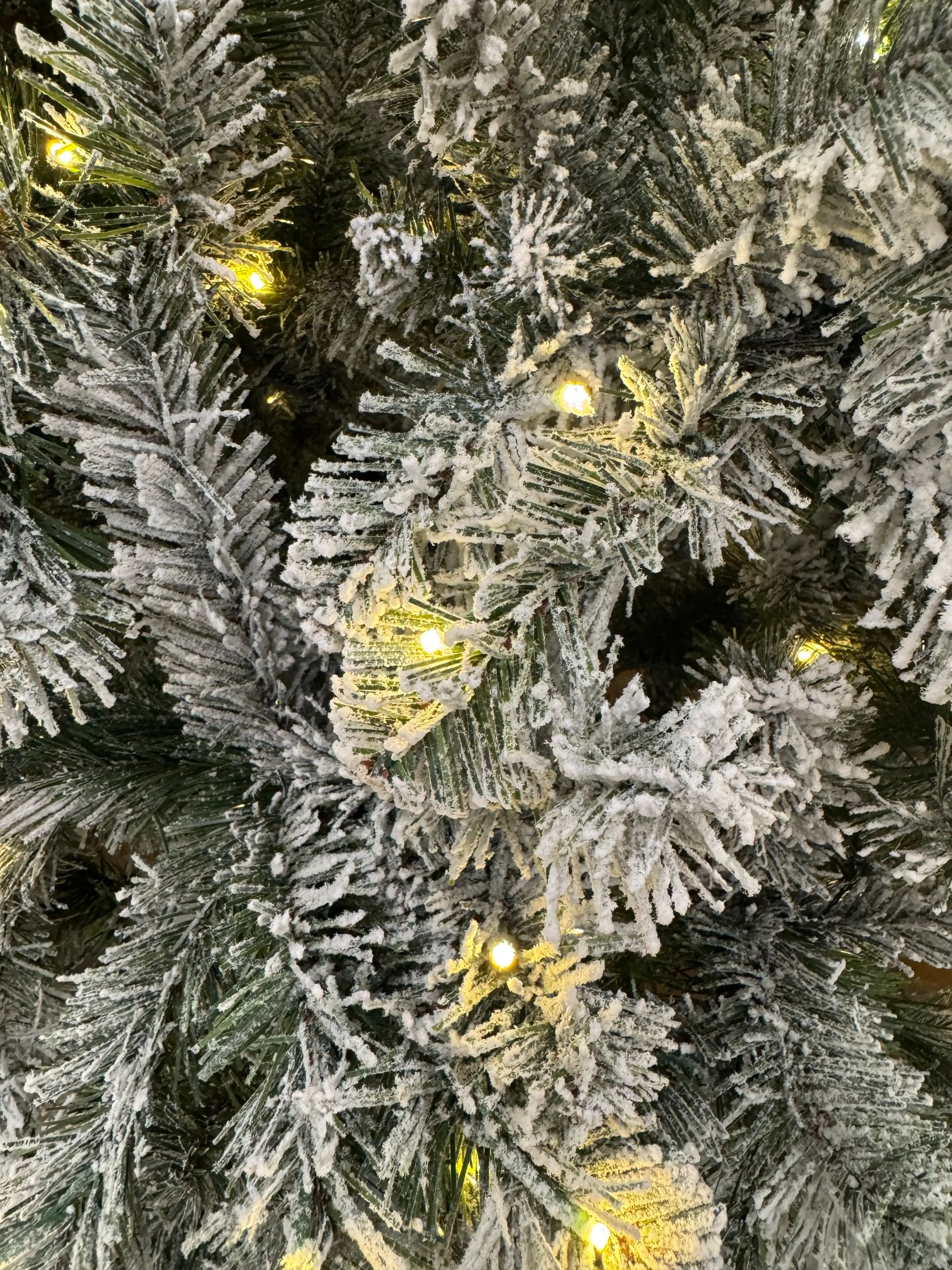 Dense PVC spruce branches with heavy white flocking, warm white mini bulbs distributed throughout, full coverage