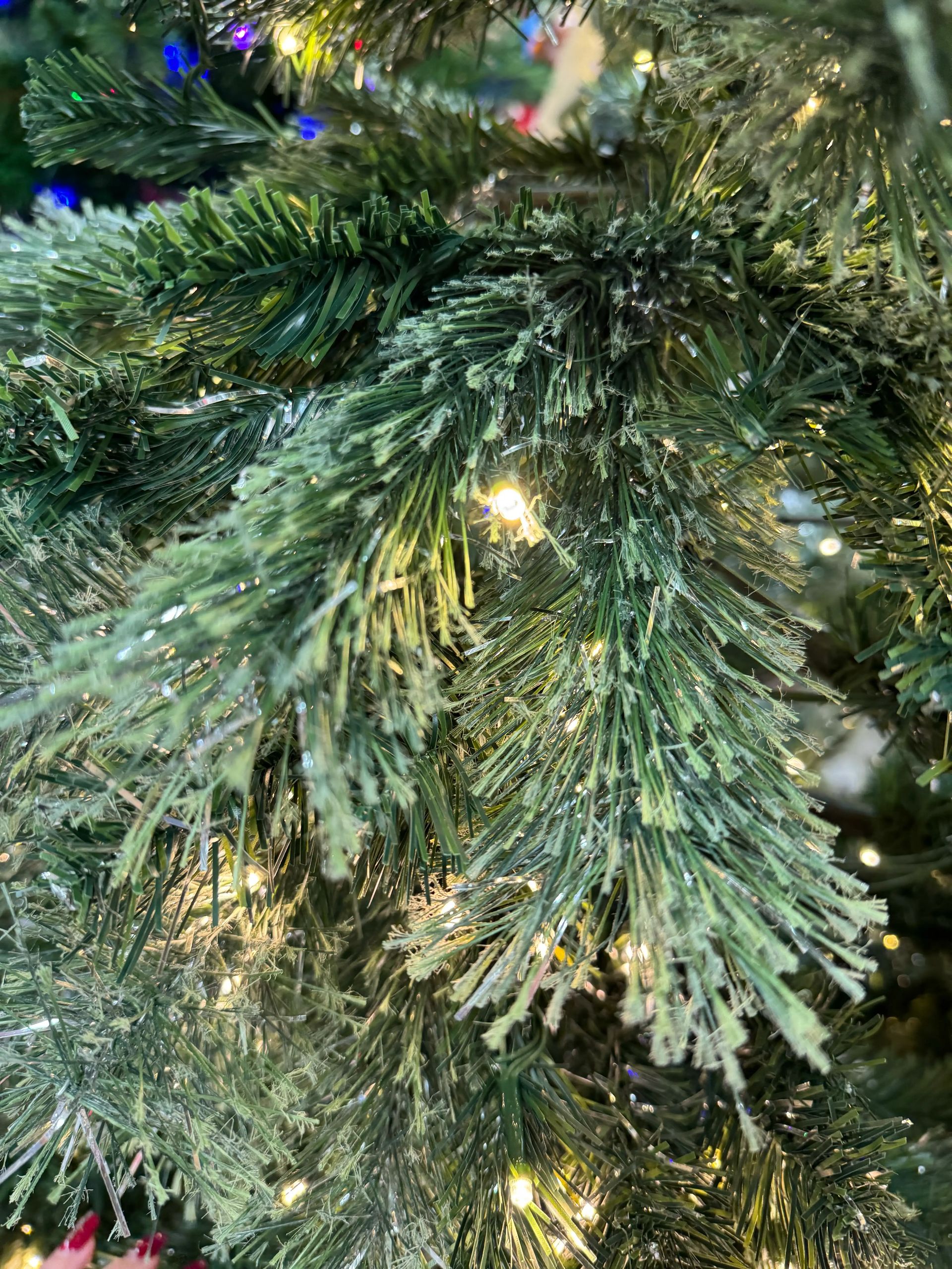 Close-up of PVC pine needles with silver tinsel strands woven throughout, warm white mini bulbs visible in branches