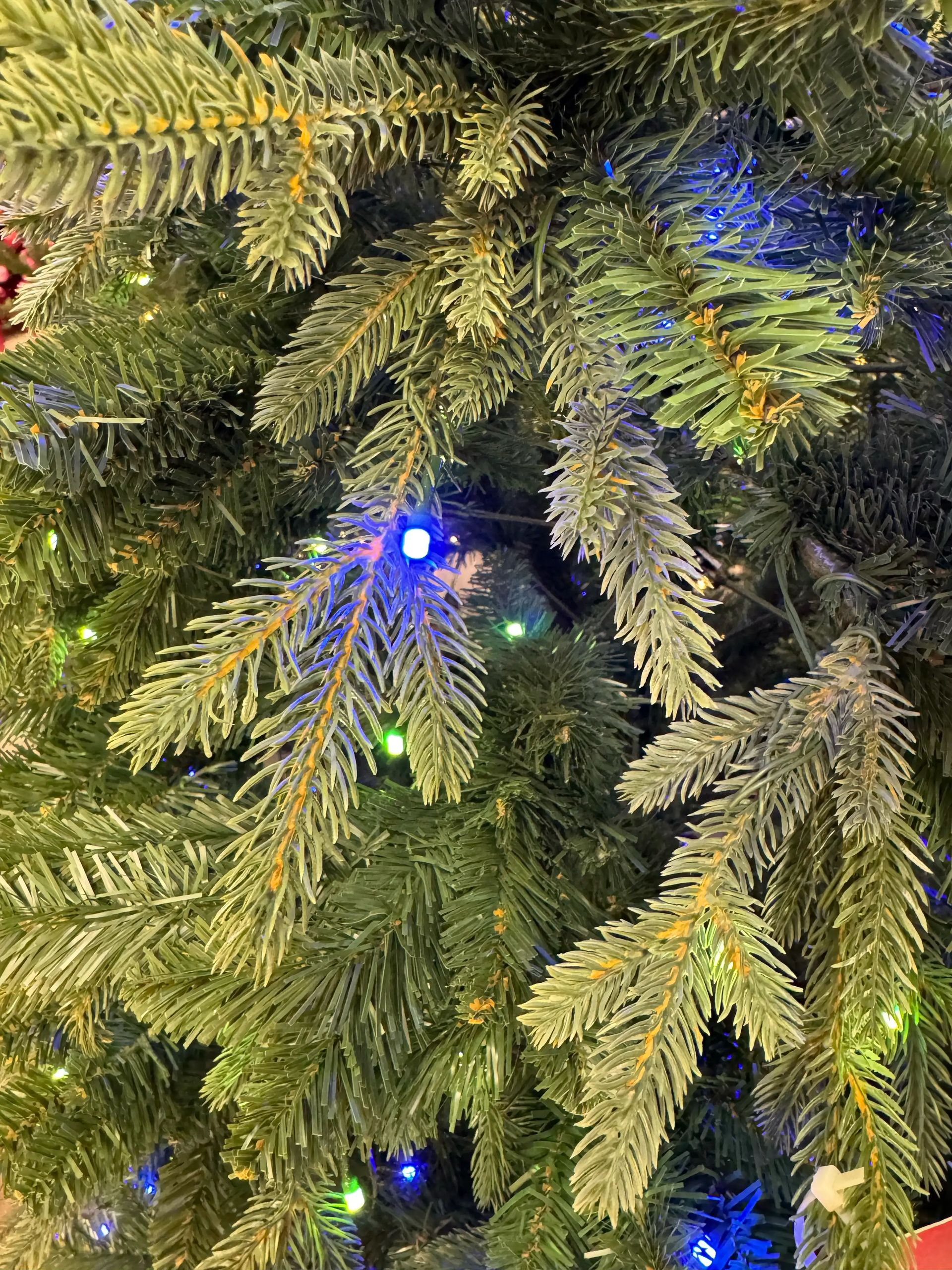 Close-up of spruce-style branches with mixed PVC and PE needles, sparse blue and green LED coverage, visible gaps between branches, modest fullness.