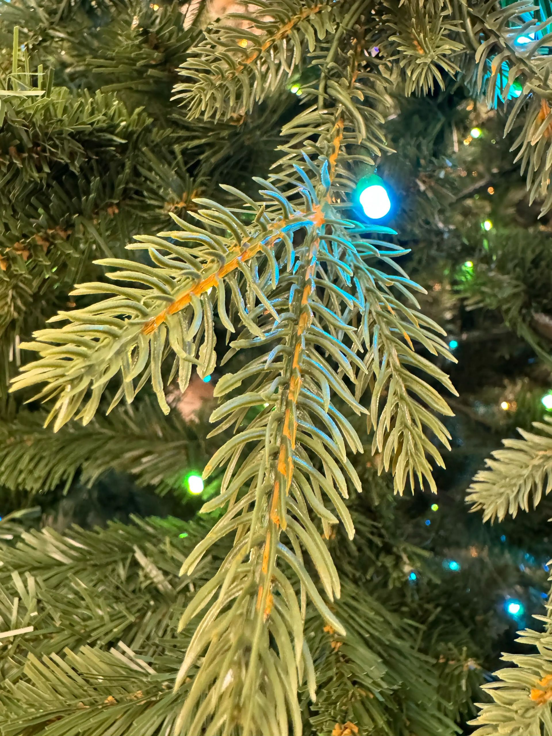Close-up of spruce-style branch with mixed PVC and PE needles, blue and green mini lights, sparse needle coverage with visible gaps and brown branch showing