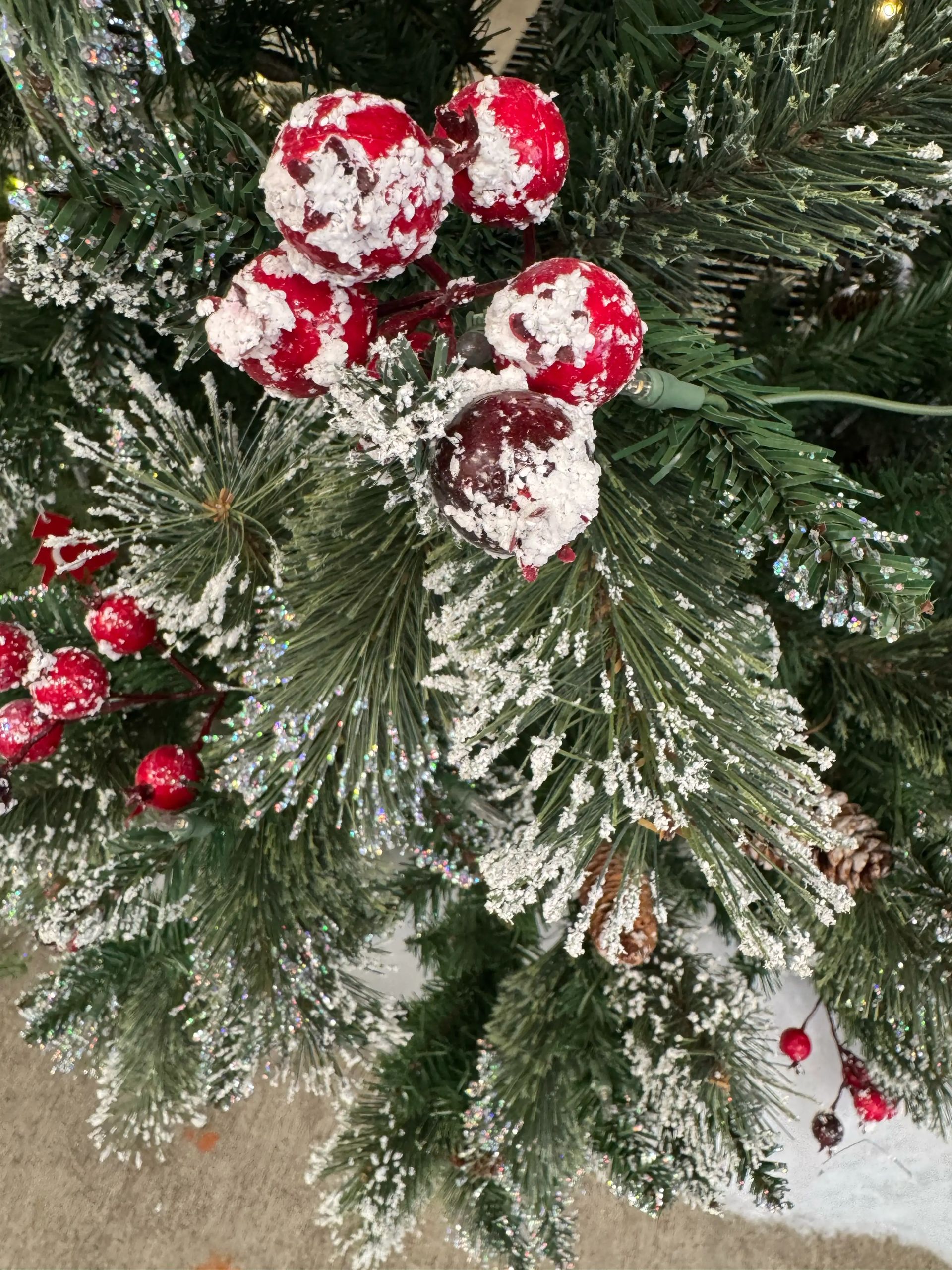 Frosted pine needles with white glitter, red berries dusted with snow effect, warm LED lights visible in background