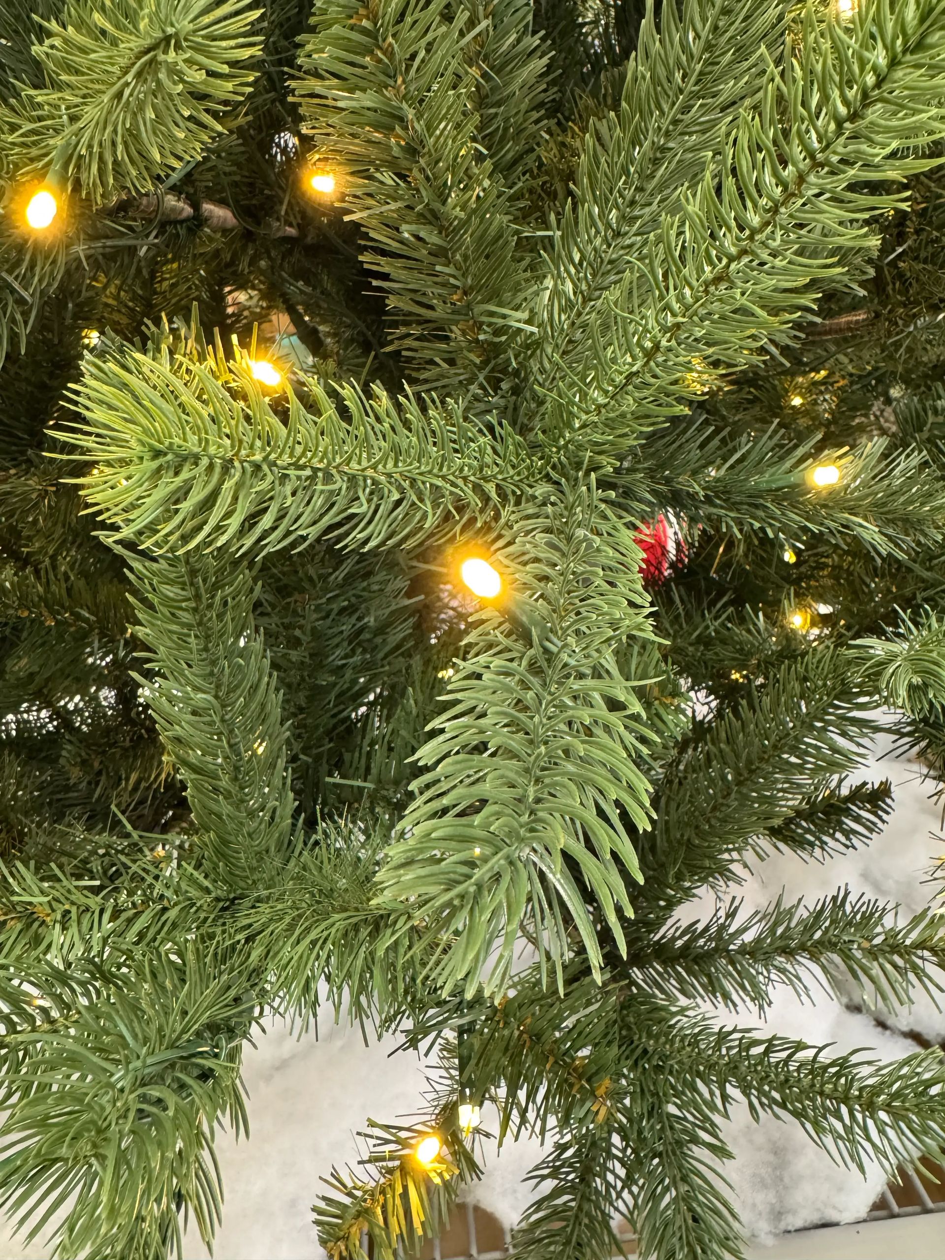 Mixed PVC/PE fir needles in green tones, warm white LED lights spaced throughout, small red pinecone ornament visible