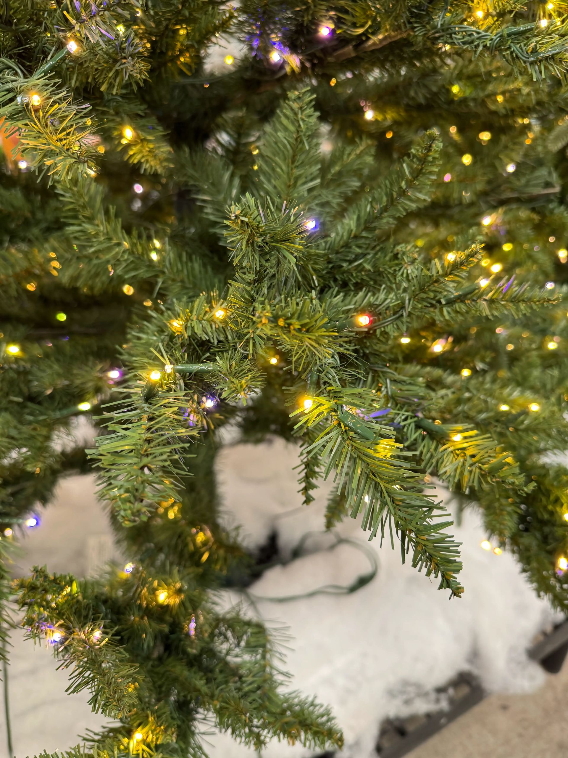 Close-up of PVC pine branches with multicolor LED lights, moderate density with some visible gaps between needles