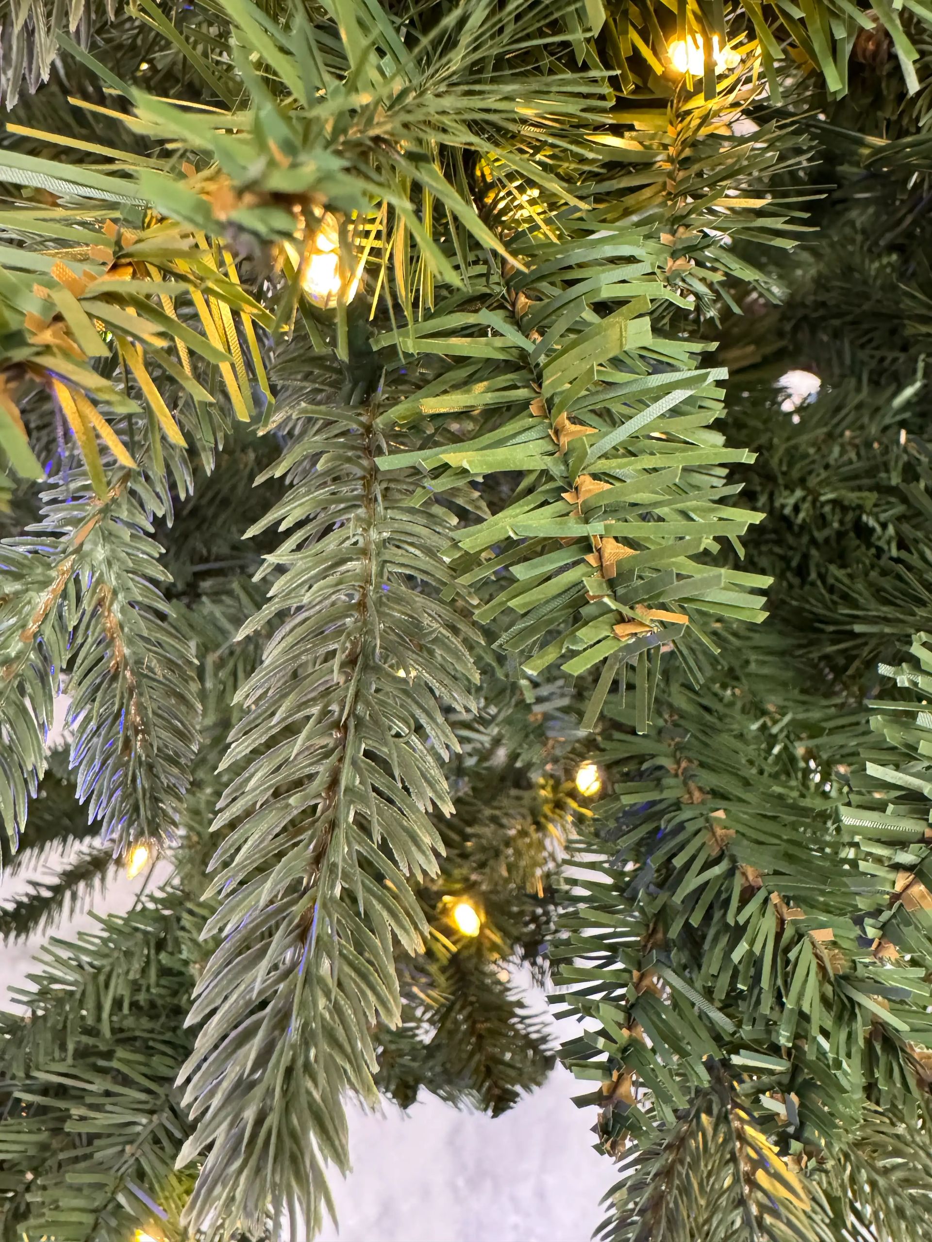 Mixed PVC and PE fir needles, moderate density with some gaps, warm white mini bulbs visible throughout branches