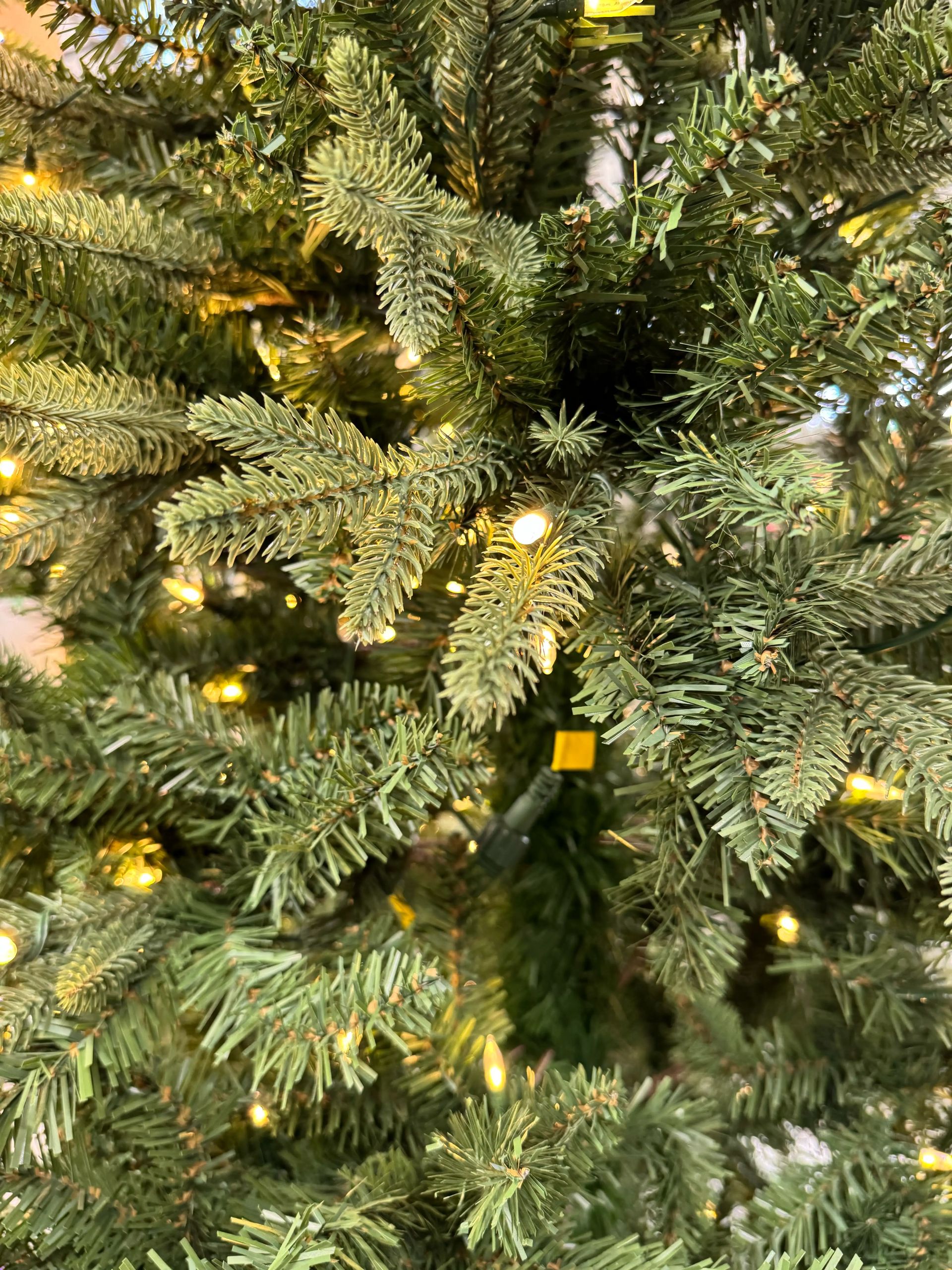 Mixed PVC and PE fir needles in green tones, warm white lights scattered throughout, moderate density with some gaps