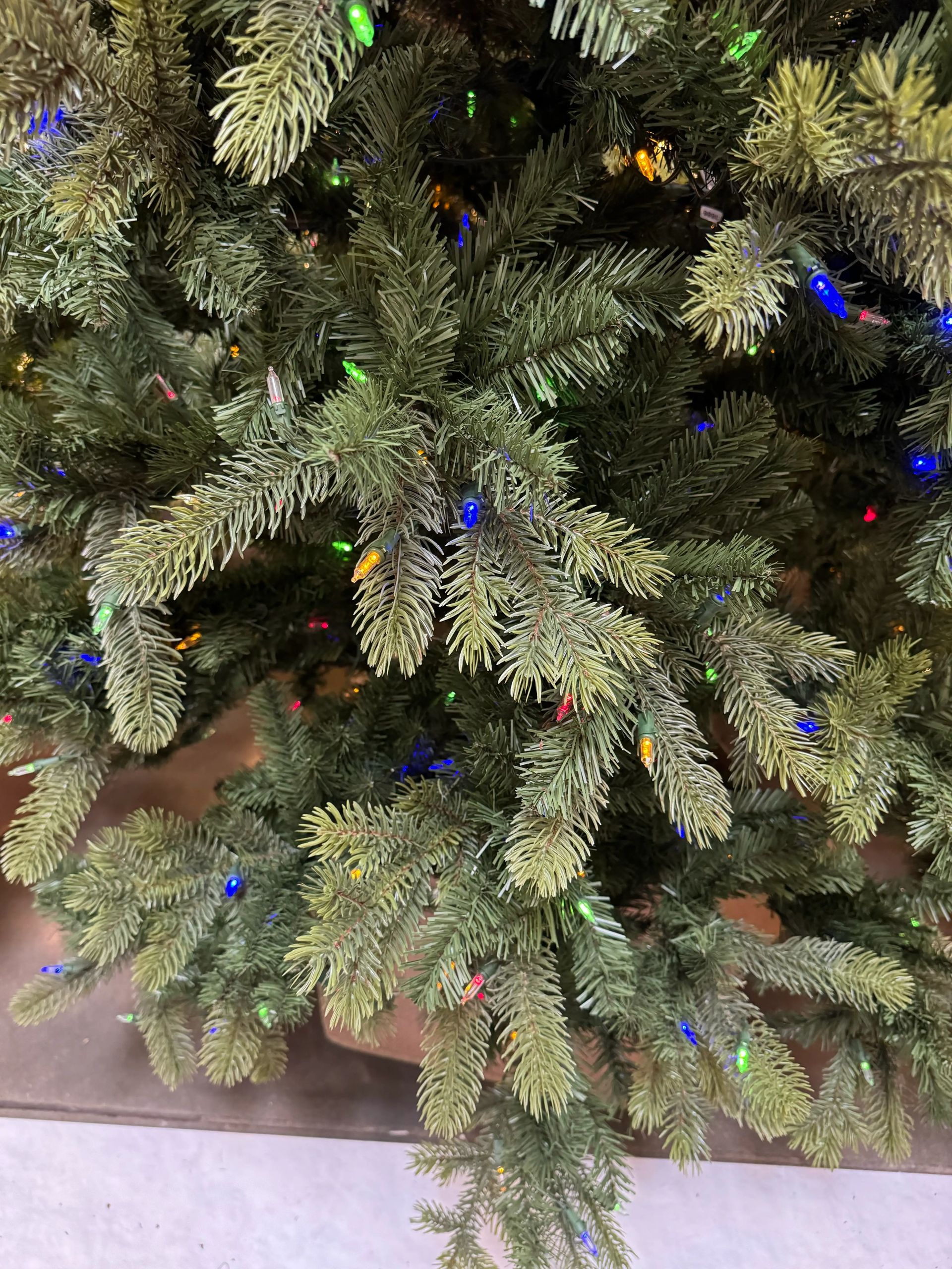 Mixed PVC/PE spruce needles with frosted tips, multicolor mini bulbs sparsely placed, brown trunk visible