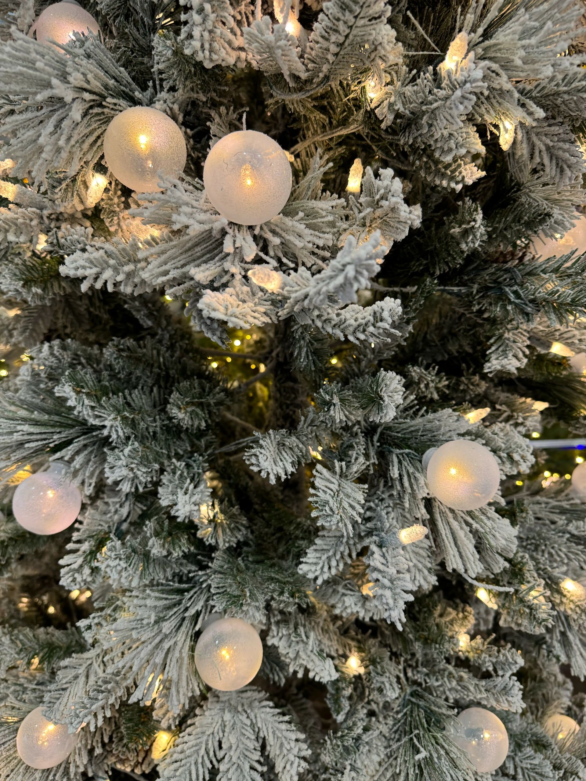 Dense flocked branches, heavy white coating, warm LED mini bulbs, frosted globe ornaments, visible green under flocking