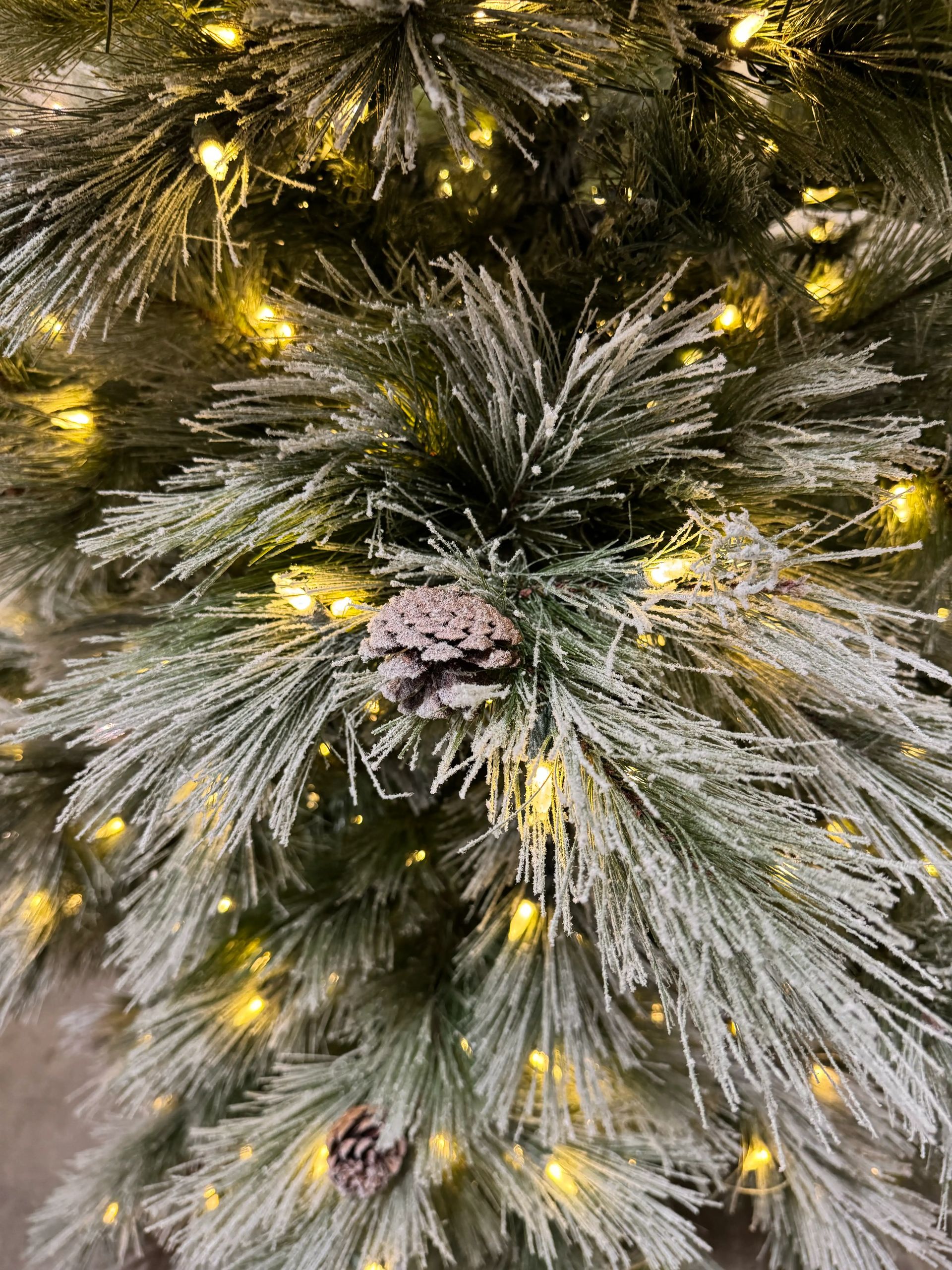 Frosted pine needles with light white flocking, warm LED lights throughout, faux pine cone attached, moderate PVC tips