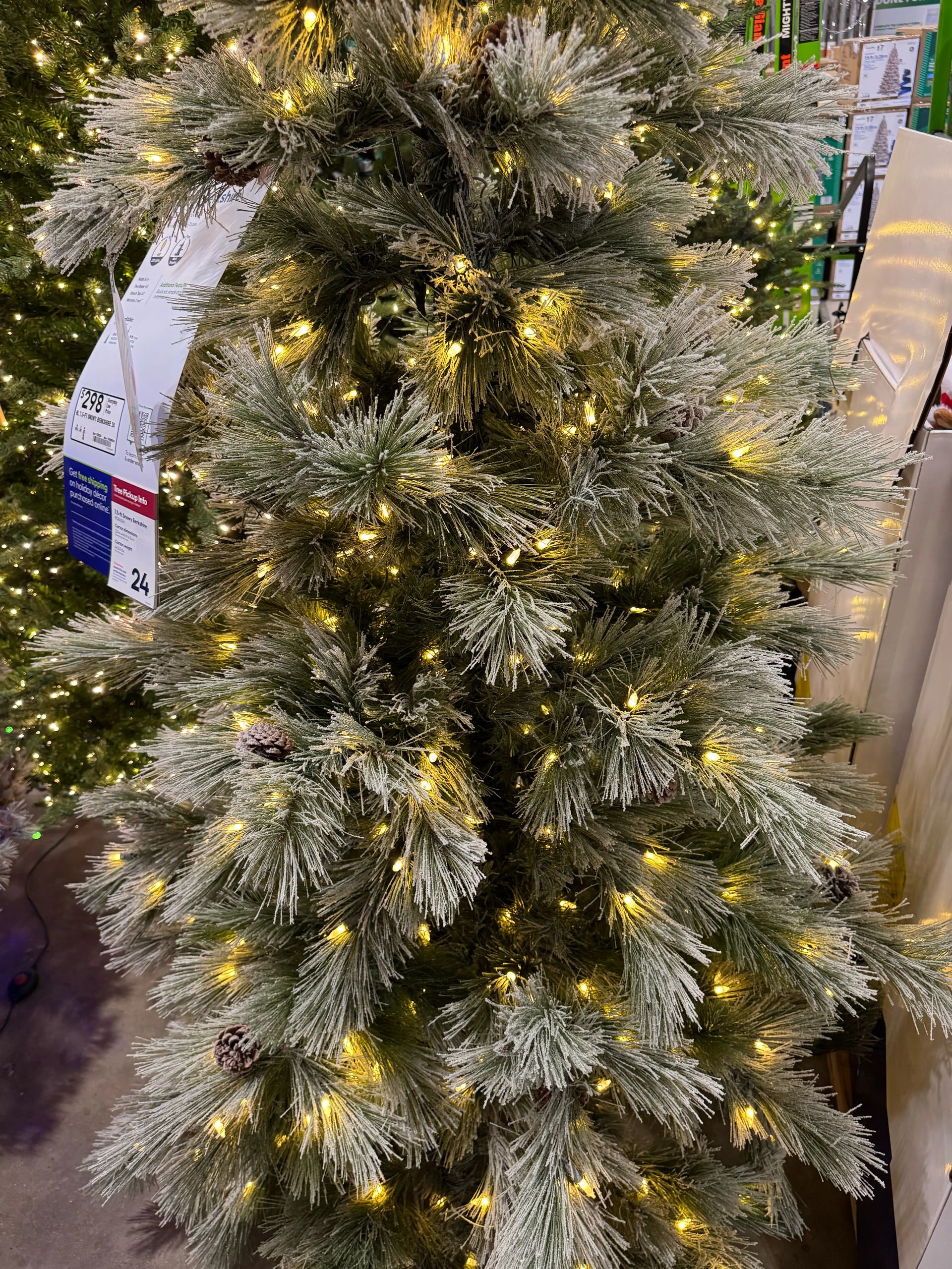 Pine-style tree with moderate PVC branches, heavy white flocking on tips, warm white LED lights throughout, visible gaps