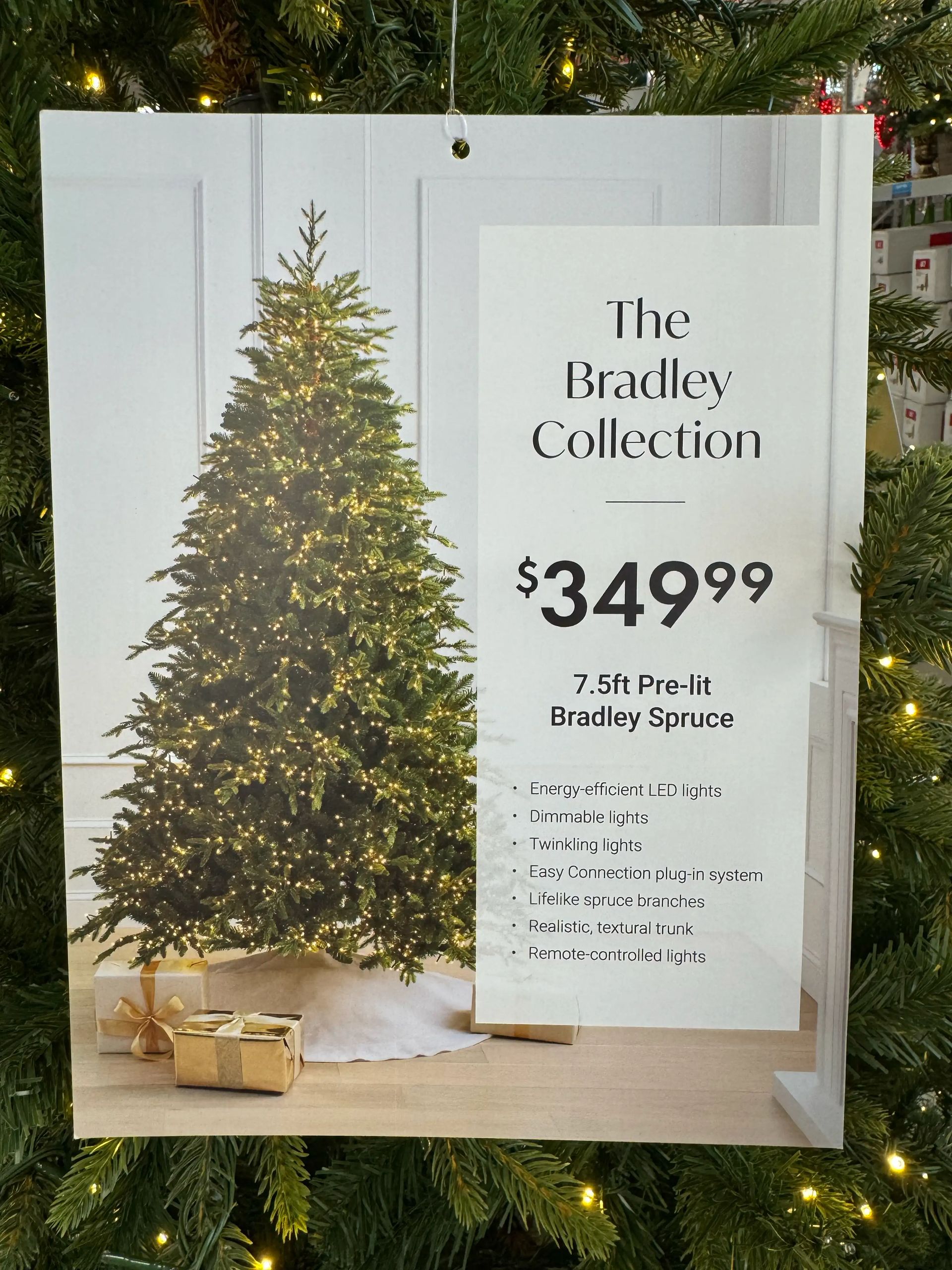 Product sign for 7.5ft pre-lit Bradley Spruce at $349.99, listing LED features, dimmable/twinkling lights, remote control